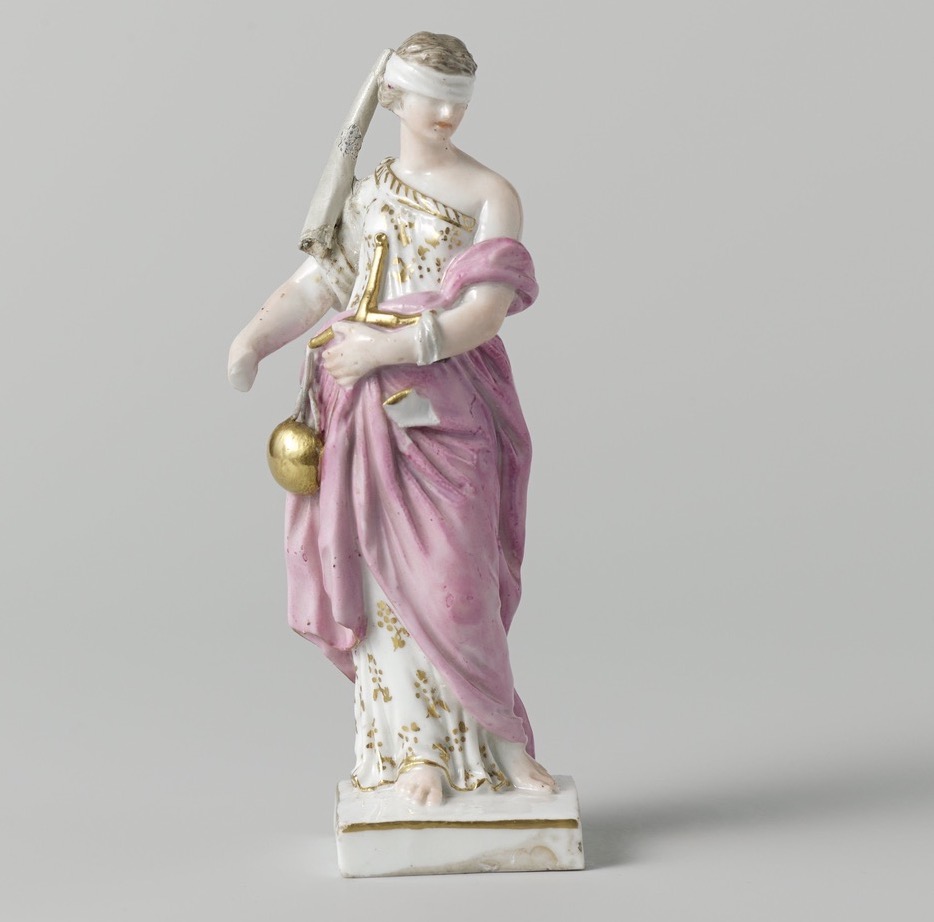 Porseleinen beeldje van Vrouwe Justitia: vrouw met een roze gedrapeerde jurk en een witte blinddoek rond haar ogen